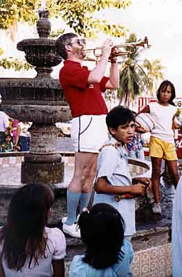 Children watch Glen play while standing on the ledge around an ornamental fountain.