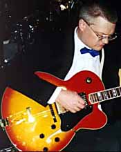 Dressed in black and white with blue bow tie, Carl plays a red and yellow guitar. Bigger picture is 22K.
