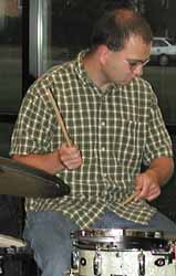 Jim sight-reads a chart at his left while playing the band's drum set.