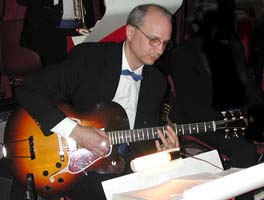 Dressed in a black suit with a blue bow tie, Jim reads music on one of the band's red and white music stands.