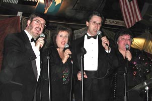 The quartet members each hold mics while singing.