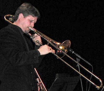 Dressed in black, Rich plays trombone into the microphone.